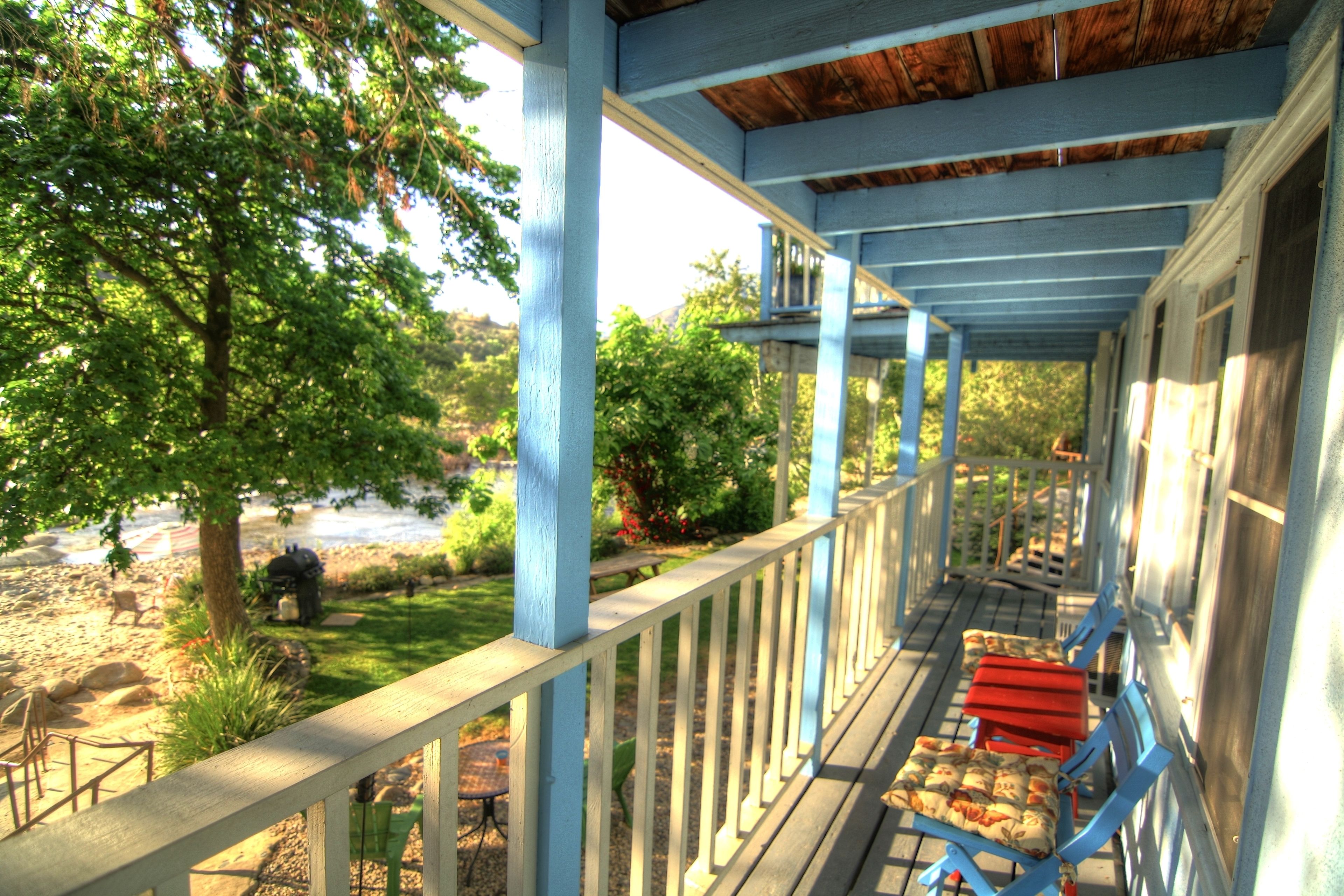 A covered porch with blue railings and red cushioned chairs.