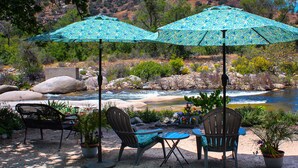 Two outdoor seating areas with chairs and tables, surrounded by potted plants and overlooking a river.