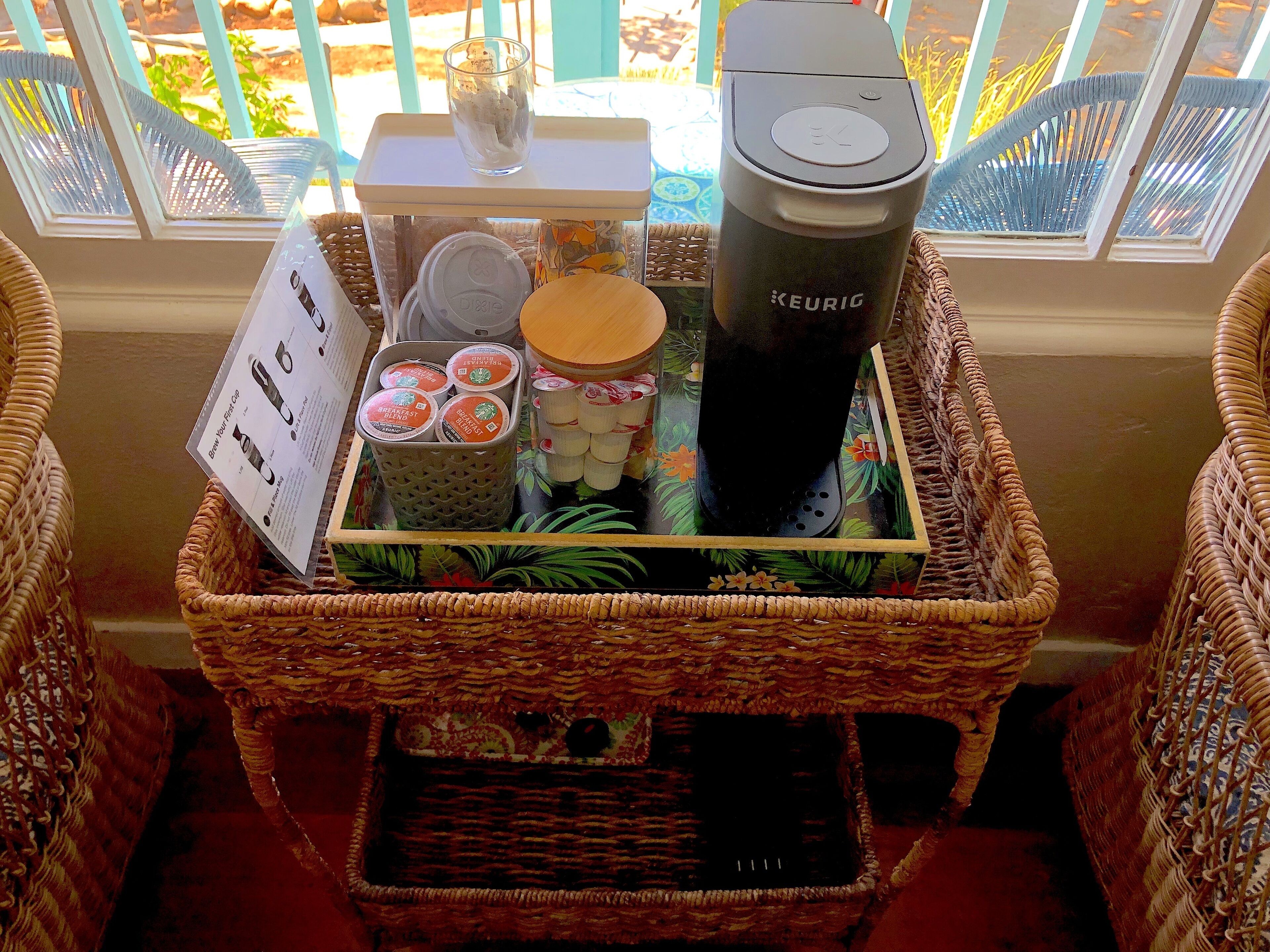 A wicker basket with a Keurig coffee maker, a glass of iced coffee, and a tray with a menu and coffee cups.