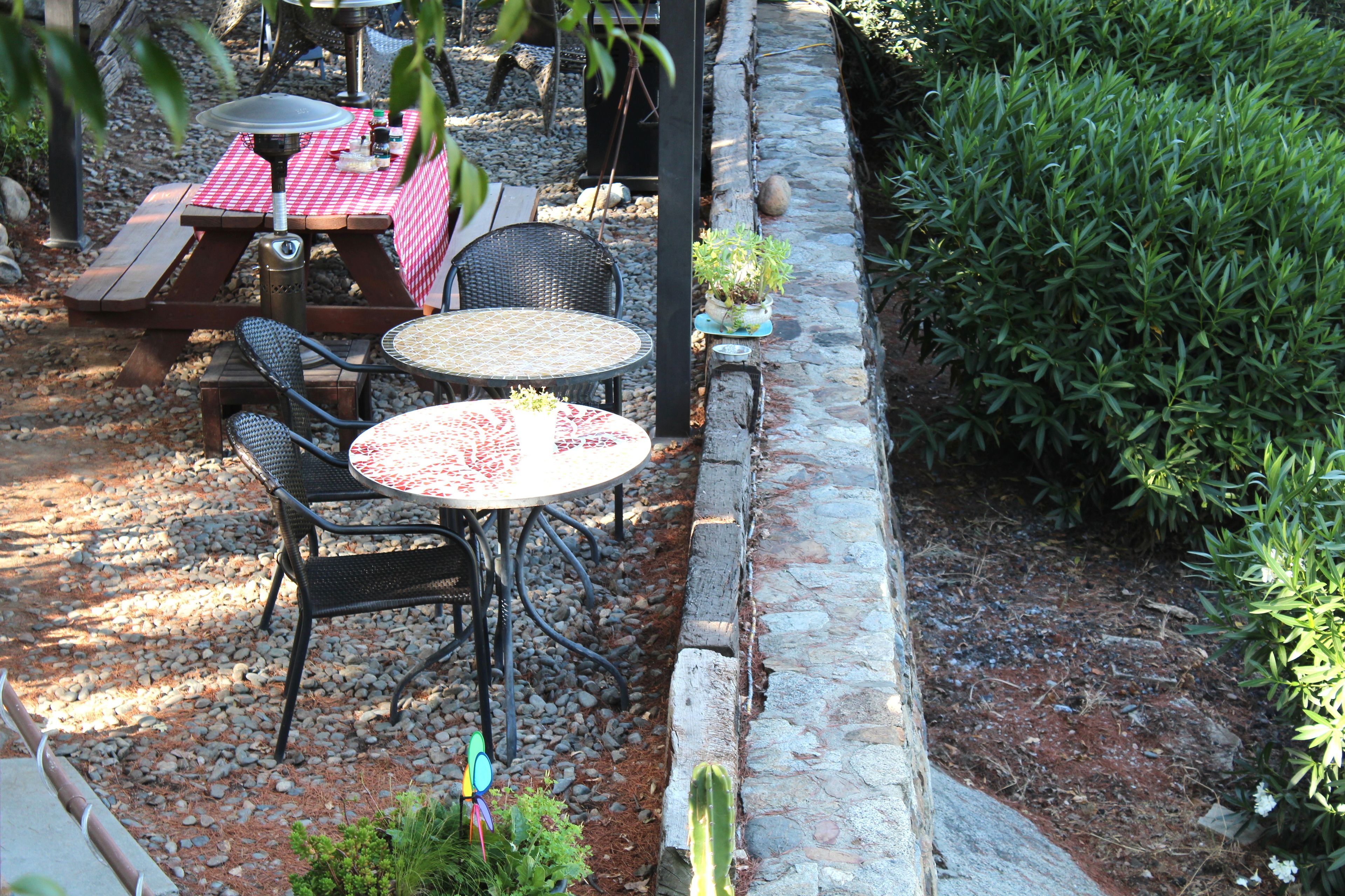 An outdoor patio area with a picnic table and chairs, surrounded by a stone wall and greenery.