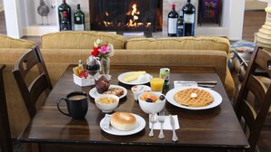 A dining table set with breakfast items, a fireplace, and wine bottles in the background. - Elm House Inn (Napa)