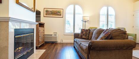 A living room with a fireplace, a sofa, and two windows with shutters.
