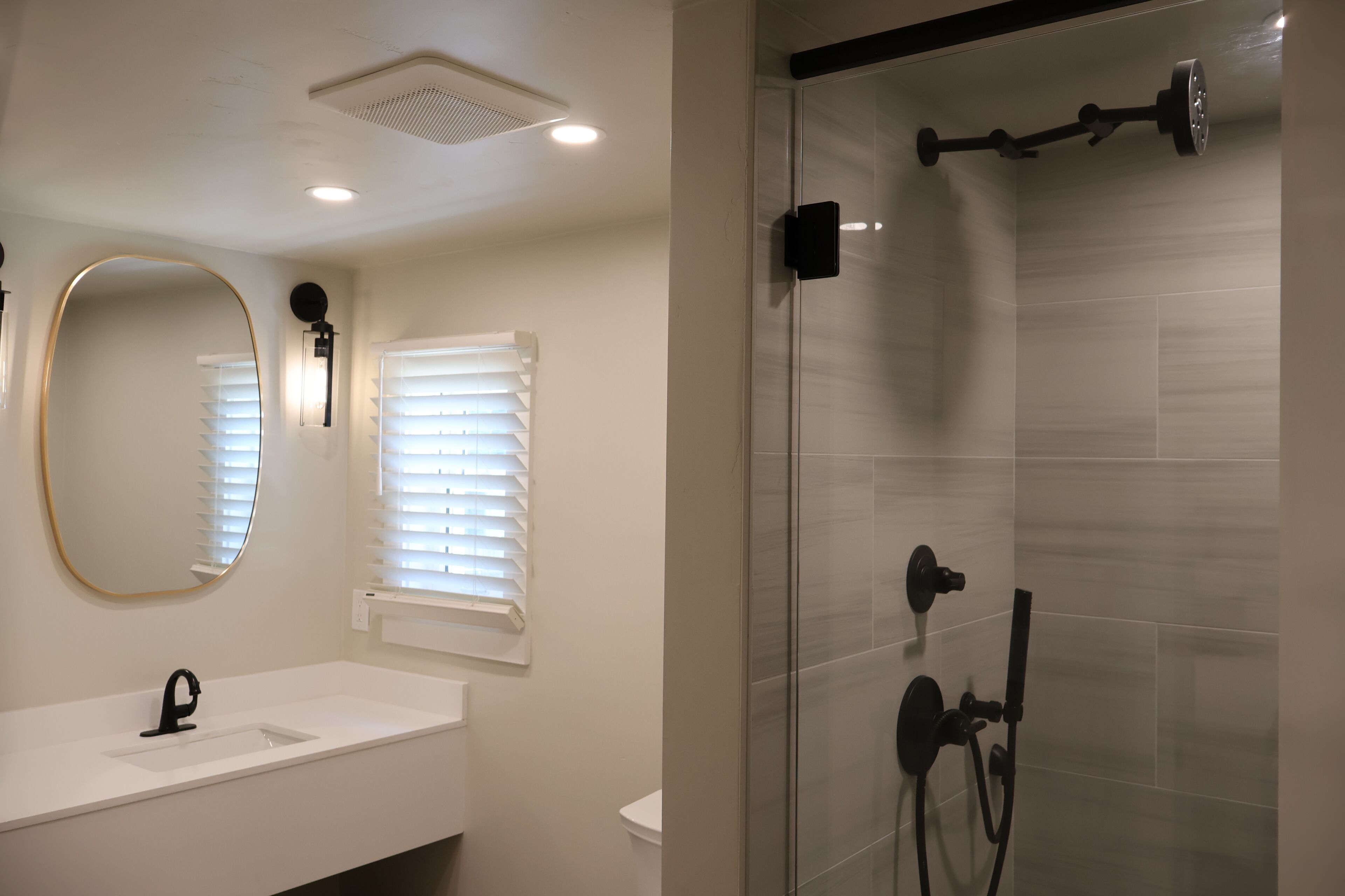 A bathroom with a white sink, a round mirror, and a glass-enclosed shower with a handheld showerhead.