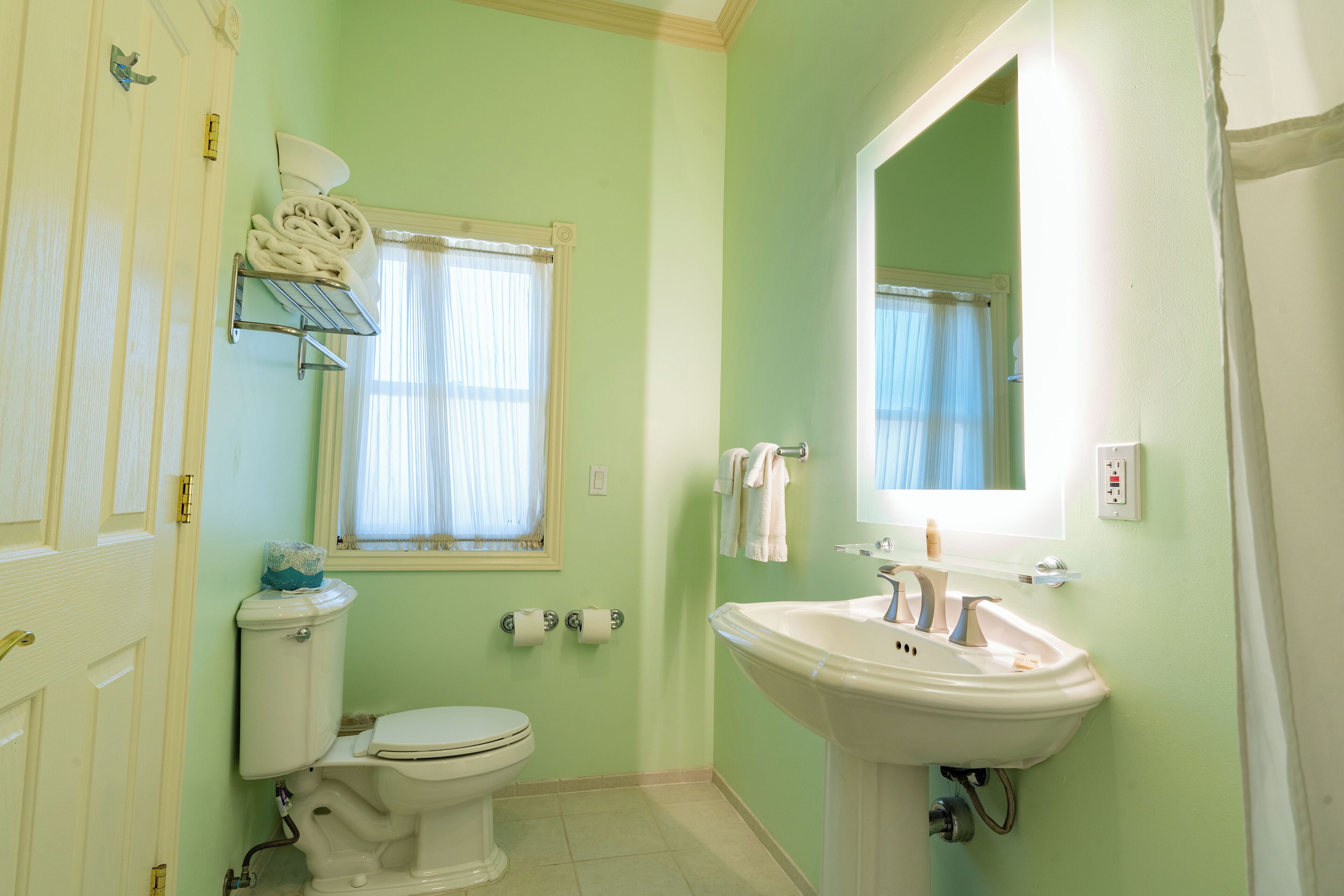 A bathroom with a toilet, sink, and a window with curtains.