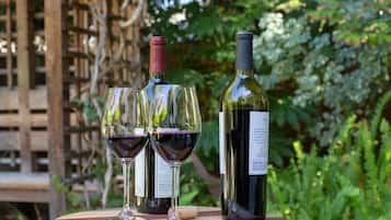 Two wine glasses and a wine bottle on a wooden table outdoors with greenery in the background.