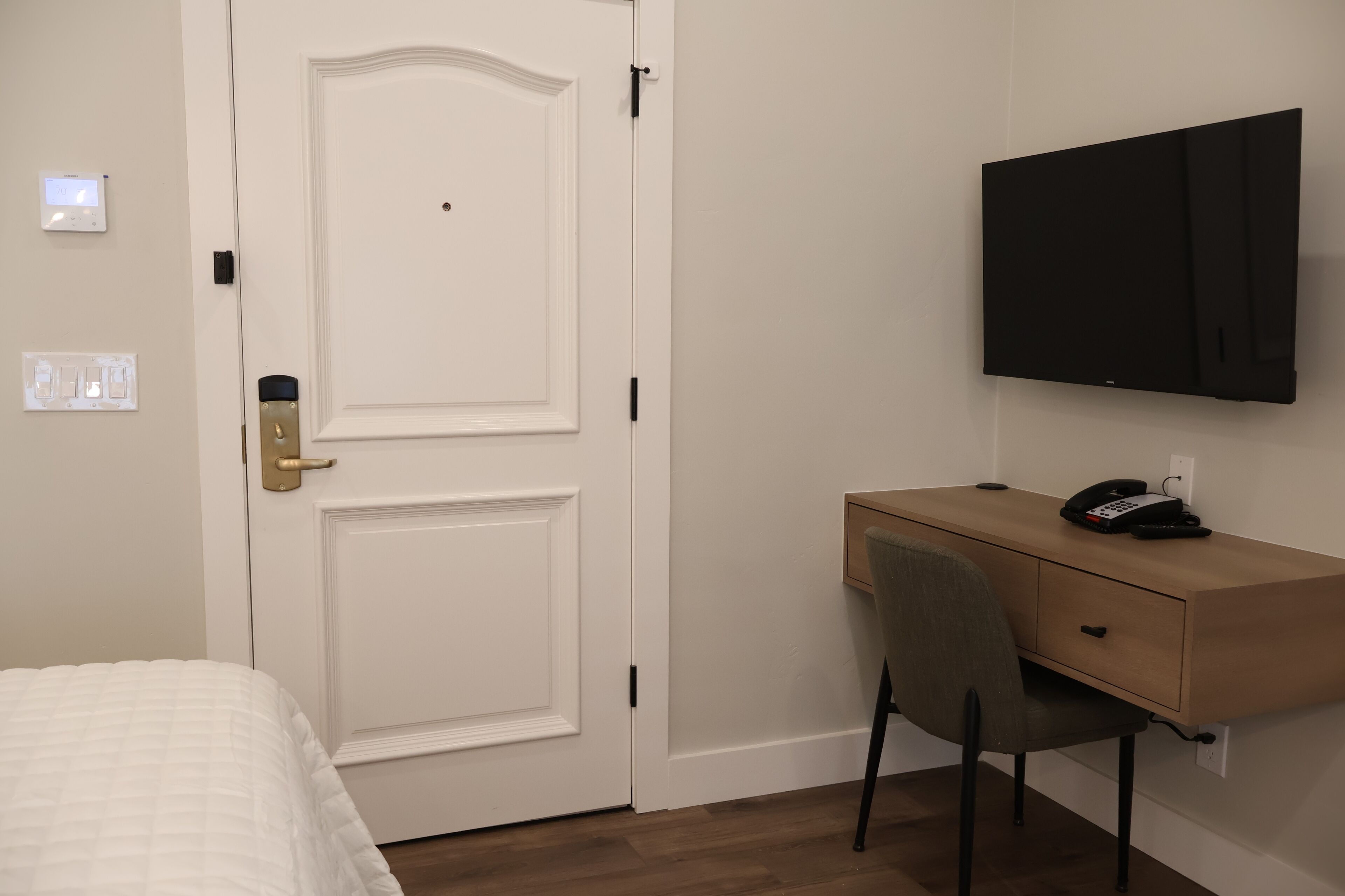 Een hotelkamer met een bed, een bureau met stoel, een wandtelevisie en een deur met slot.