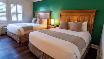 A hotel room with two beds, wooden headboards, a green accent wall, and a window with blinds.