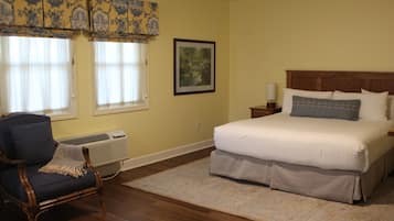 A bedroom with a large bed, a chair, a framed picture, and a window with curtains.