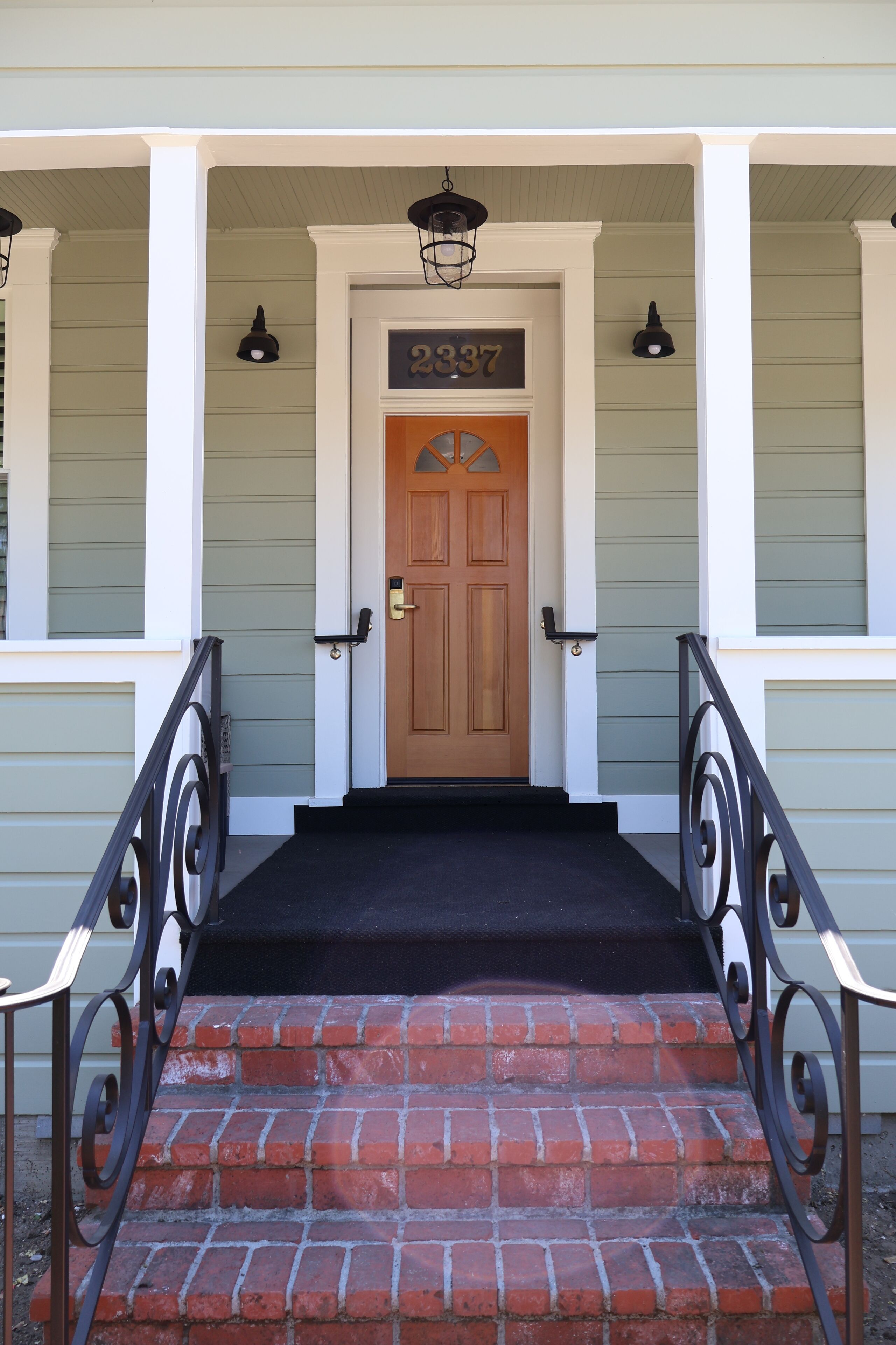 A front entrance with a wooden door, a black doormat, and a brick staircase.
