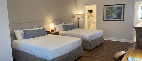 A hotel room with two beds, a desk, a chair, a lamp, and a painting on the wall.