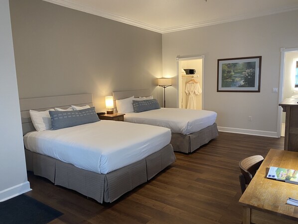 A hotel room with two beds, a desk, a chair, a lamp, and a painting on the wall.