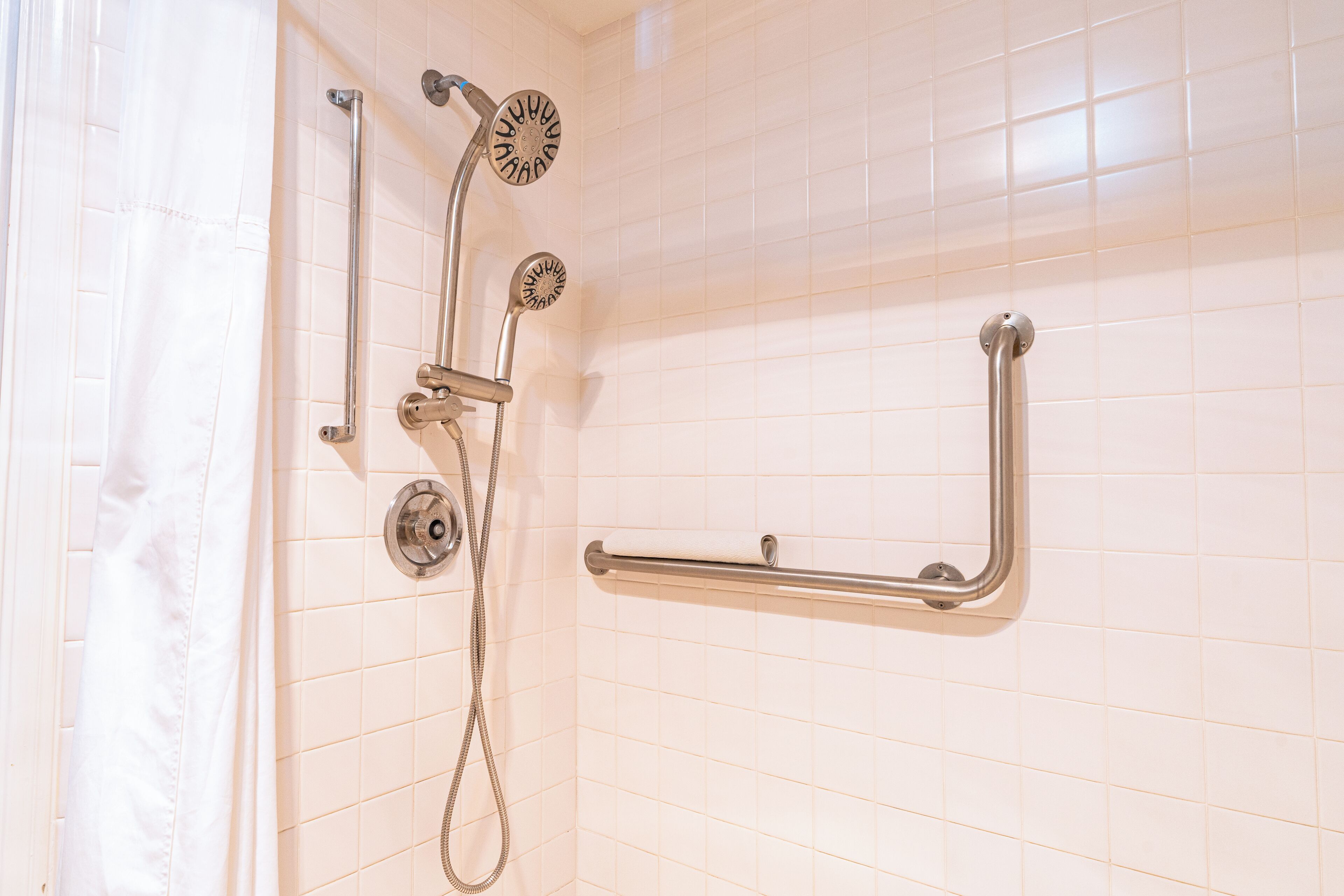 Een badkamer met witte betegelde wanden, een douche met een handdouche en een handgreep.