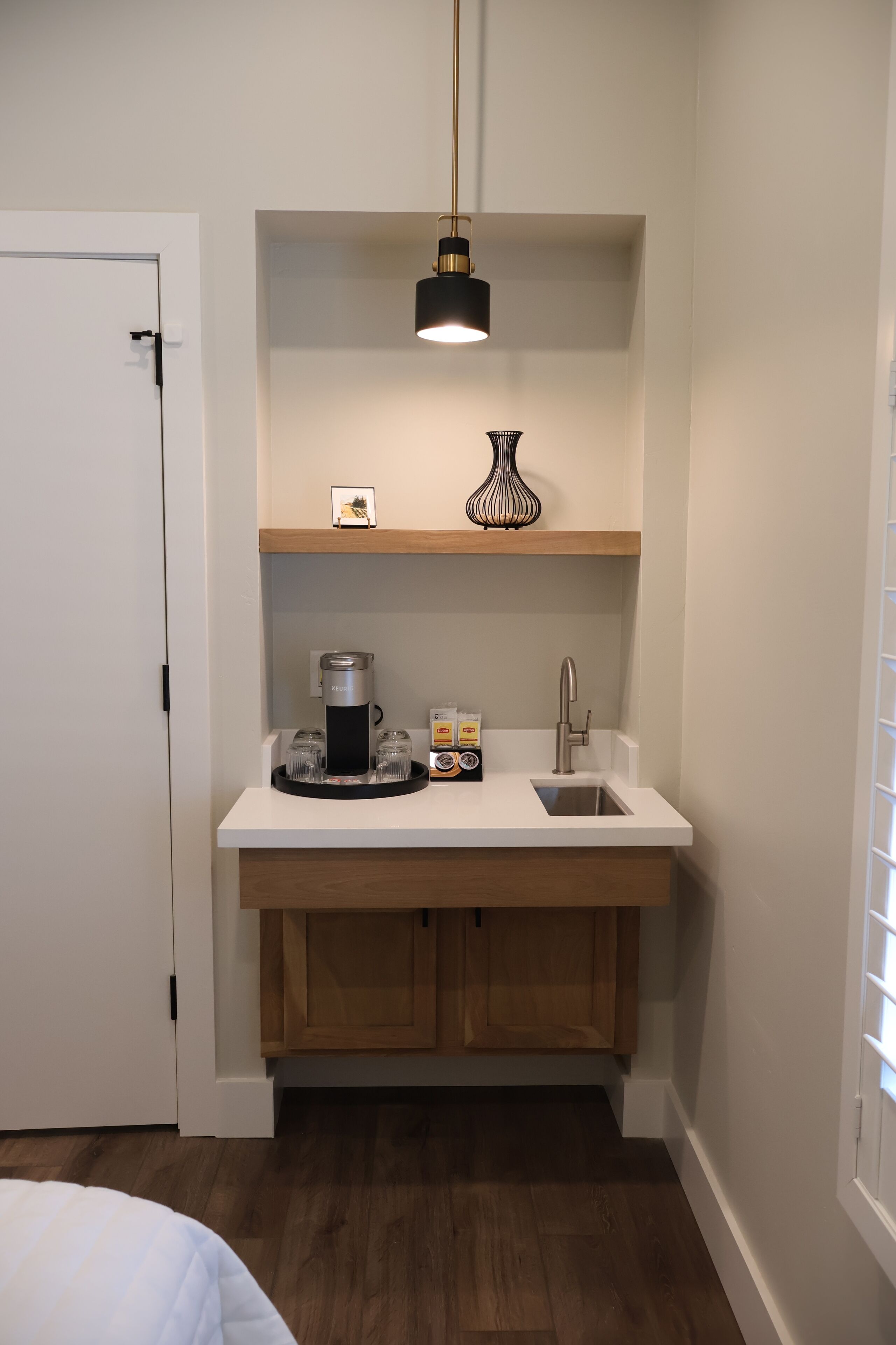 A compact kitchen with a white countertop, a coffee maker, a sink, and a hanging pendant light.