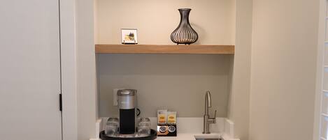A compact kitchen with a white countertop, a coffee maker, a sink, and a hanging pendant light.
