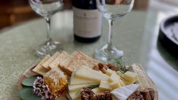 Una tabla de madera con queso, galletas y nueces sobre una mesa. Una botella de vino y dos copas se ven al fondo.