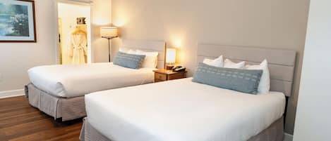 Dos camas de tamaño queen con ropa blanca y cabeceros grises en una habitación de hotel.