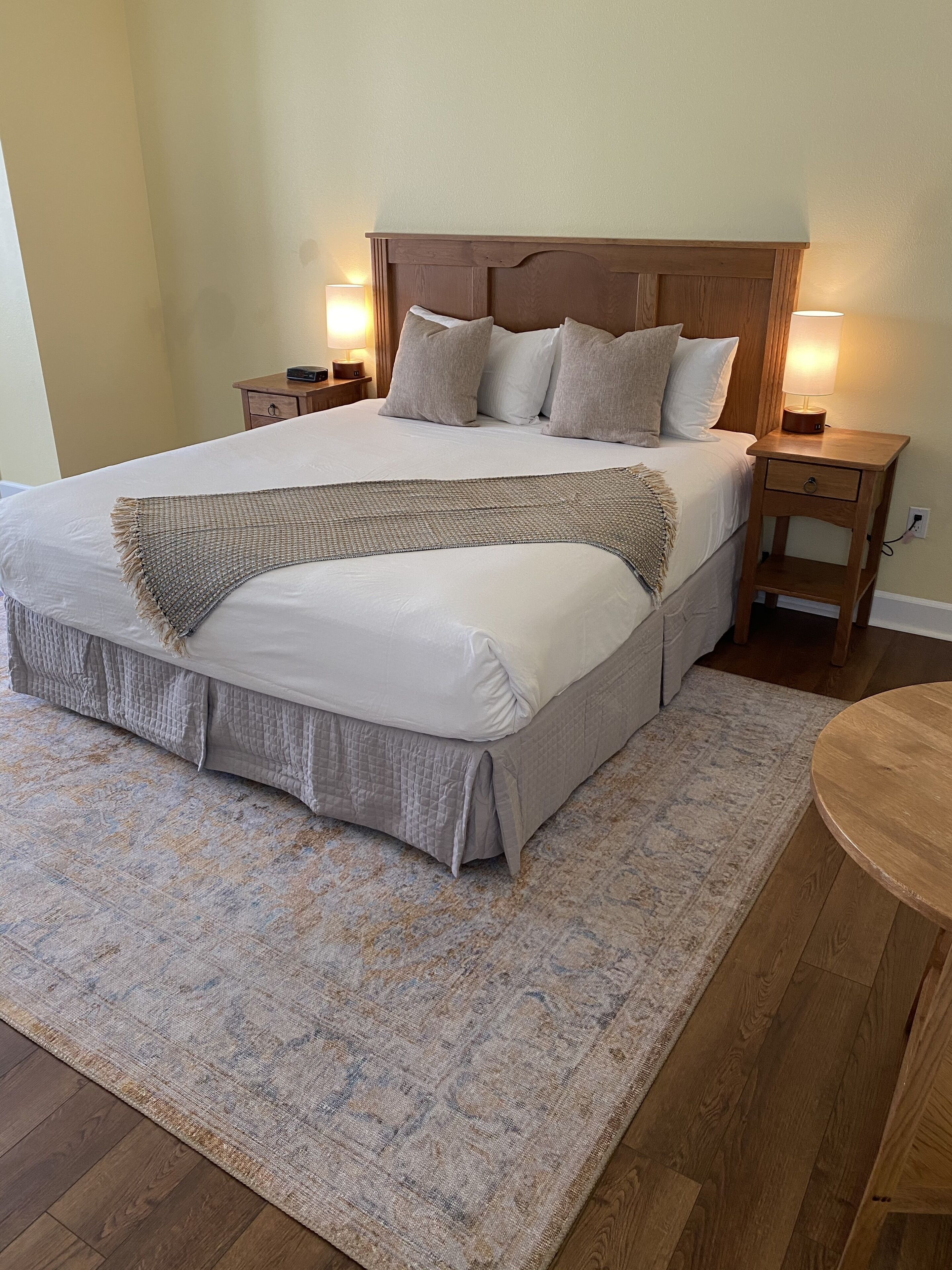A neatly made bed with a wooden headboard, two bedside tables with lamps, and a patterned rug on a wooden floor.