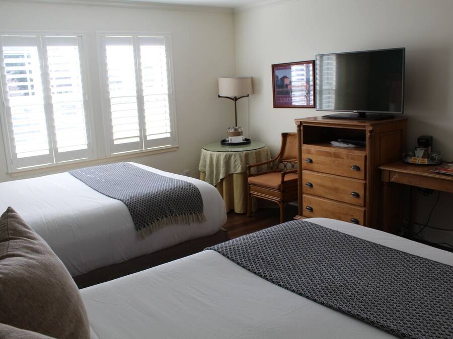 A hotel room with two beds, a desk with a television, and a small table with a lamp.