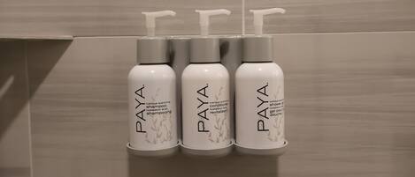 Tres botellas de champú y acondicionador PAYA en un dispensador fijado a la pared.