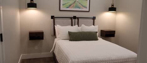 A neatly made bed with white bedding and a green pillow, flanked by two bedside tables with wall-mounted lamps.