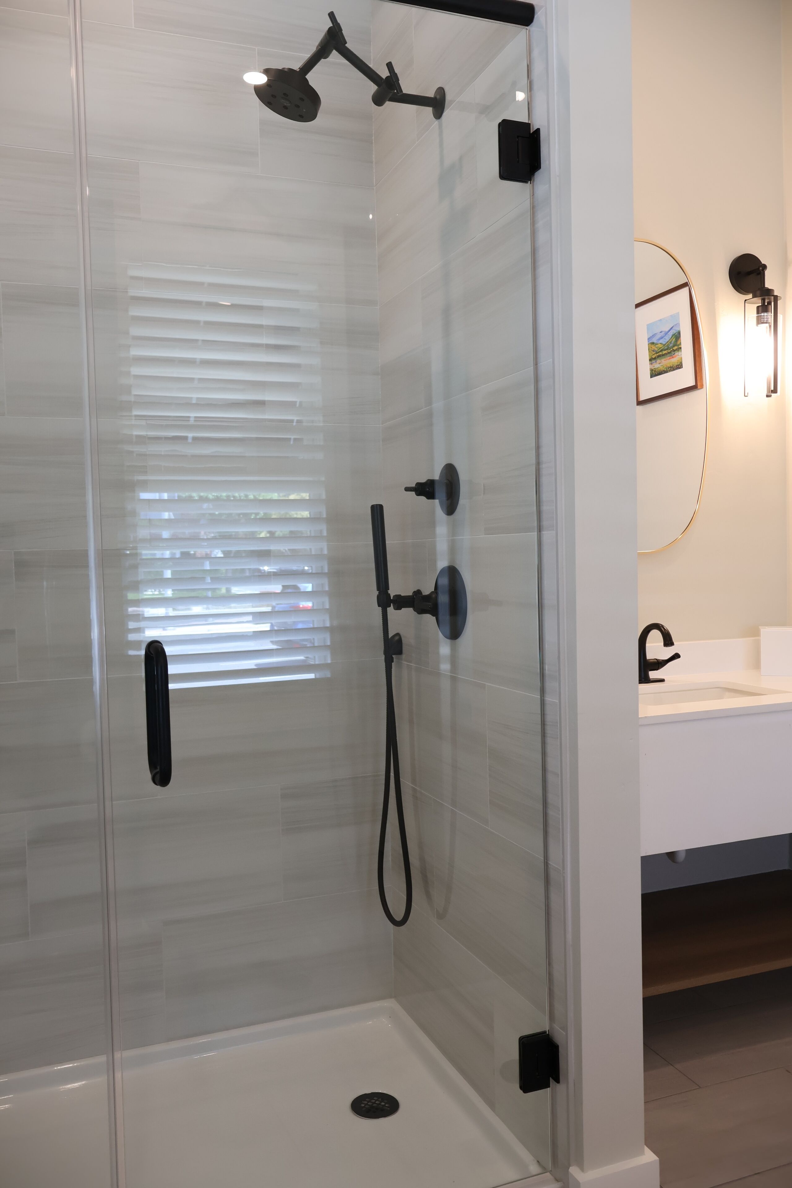 A glass-enclosed shower with a handheld showerhead, a wall-mounted faucet, and a control panel.