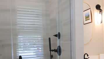 A glass-enclosed shower with a handheld showerhead, a wall-mounted faucet, and a control panel.