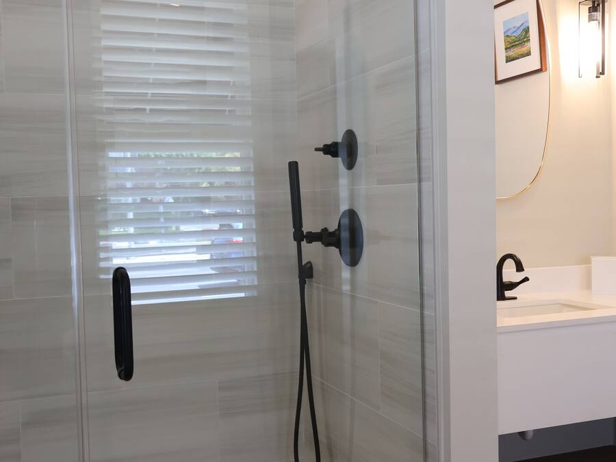 A glass-enclosed shower with a handheld showerhead, a wall-mounted faucet, and a control panel.