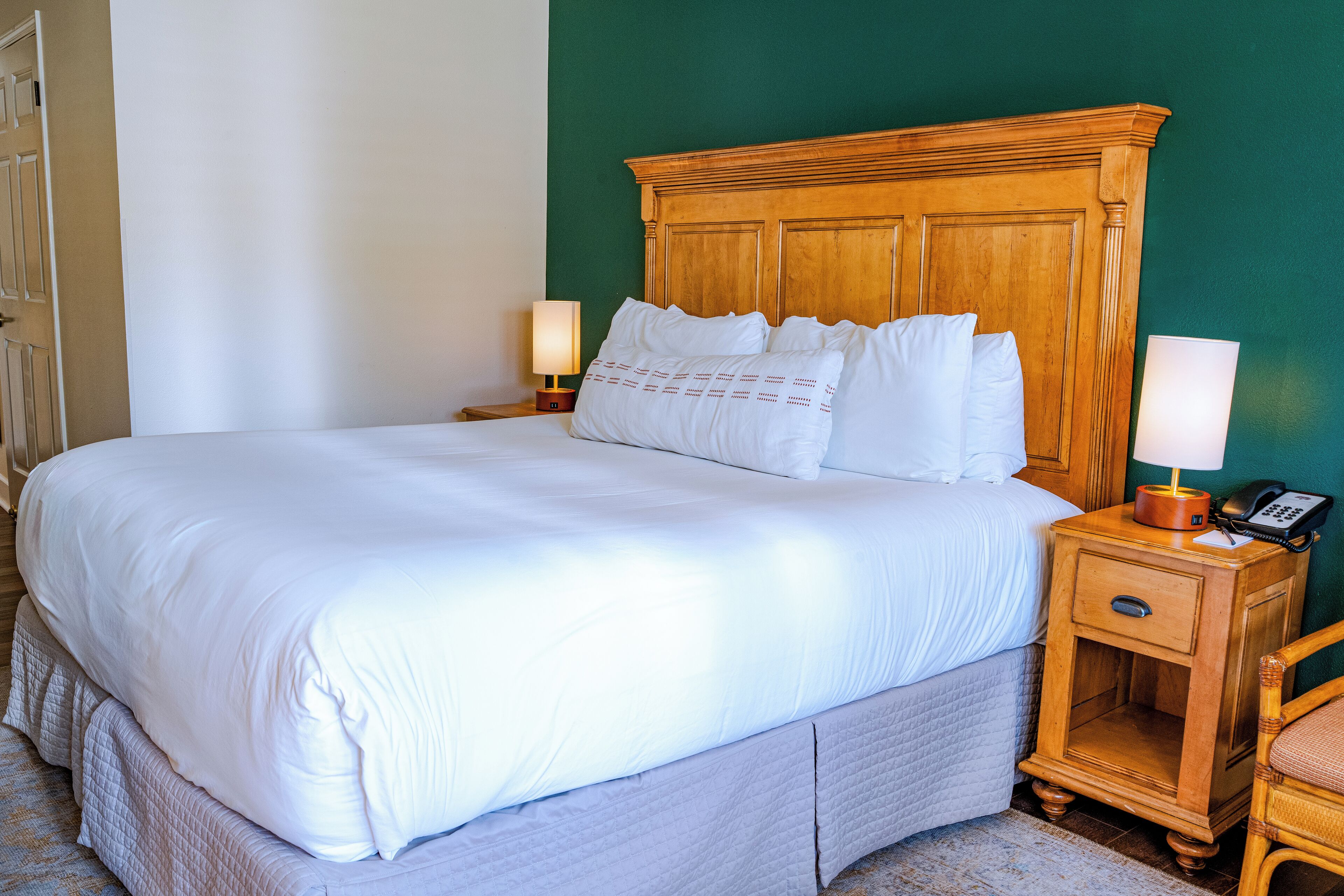 A neatly made bed with white linens, a wooden headboard, and two bedside lamps.