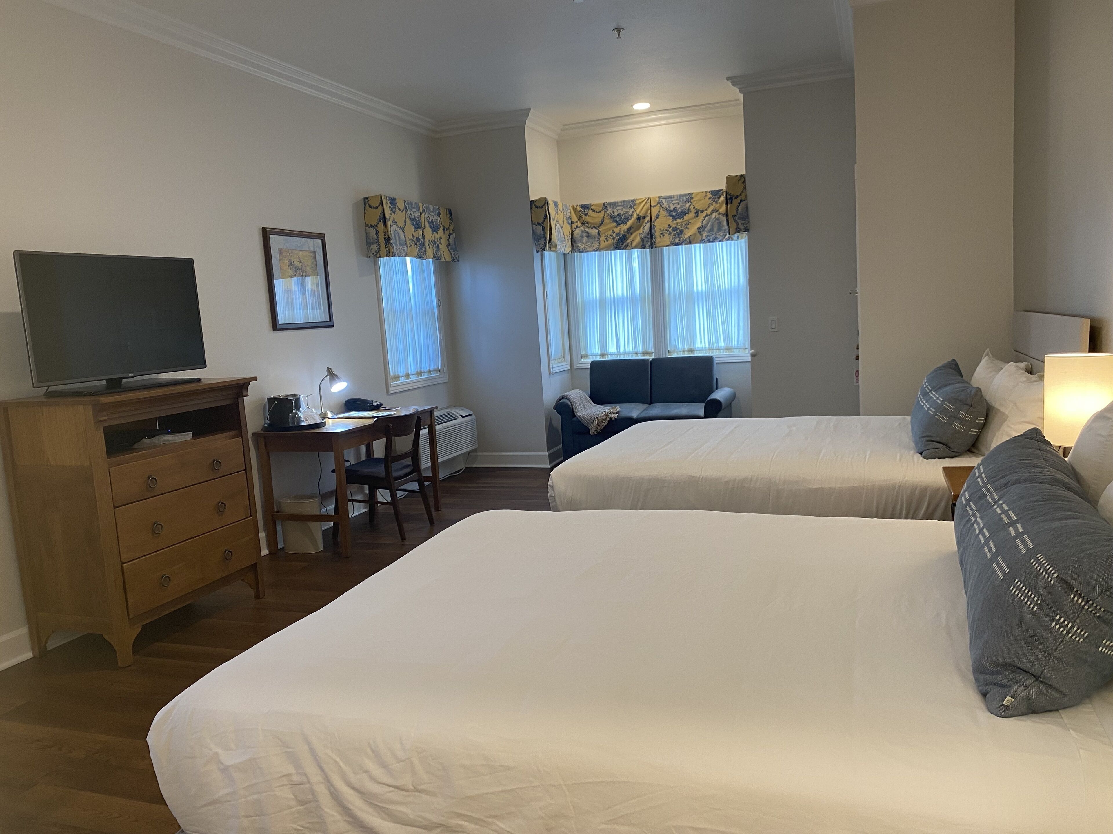 A hotel room with two beds, a desk, a television, and a chair.