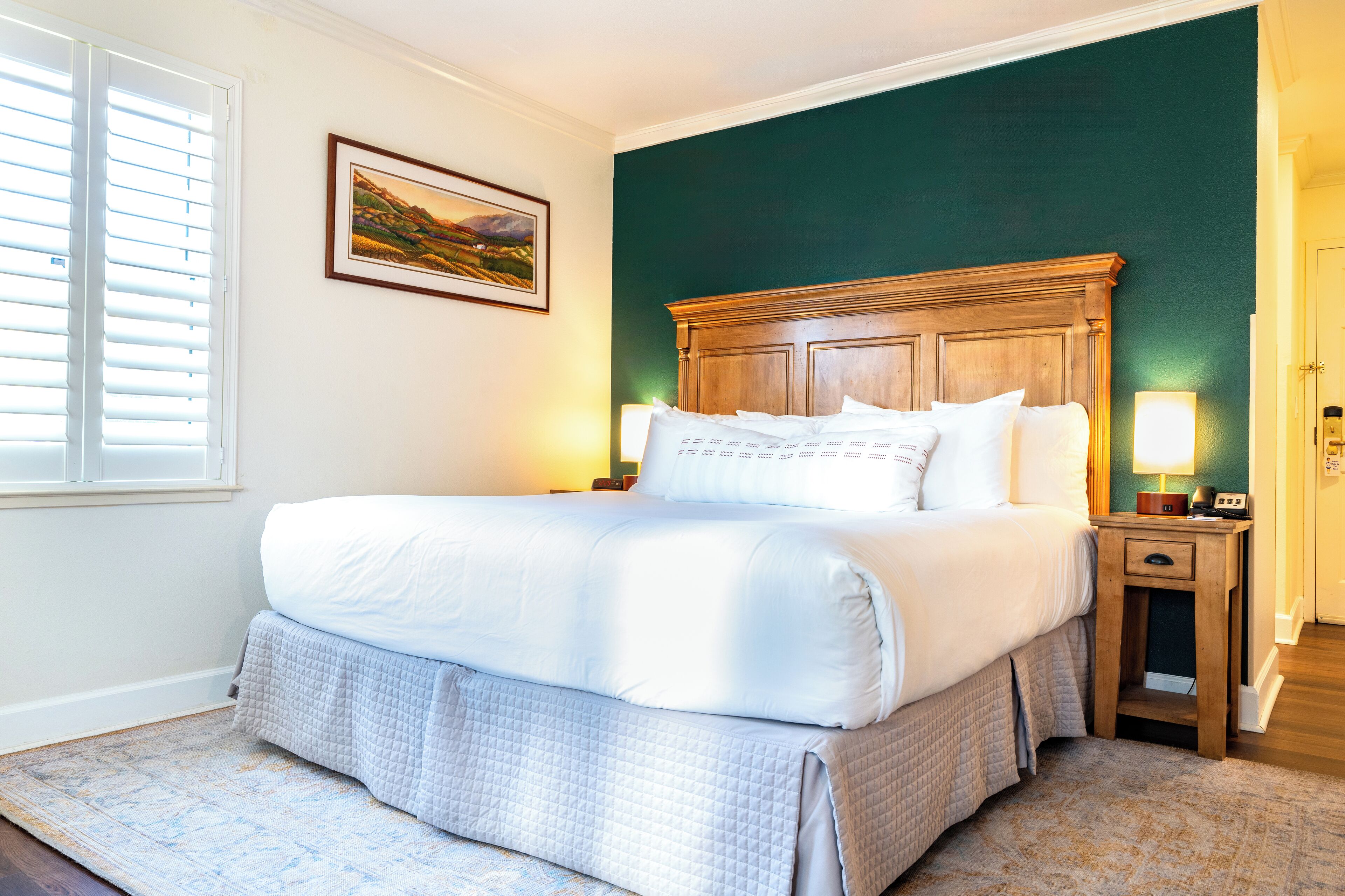 A neatly made bed with a wooden headboard, a bedside table with a lamp, and a framed picture on the wall.