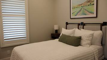 A neatly made bed with a white quilt and a green pillow, a nightstand with a lamp, and a framed painting on the wall.