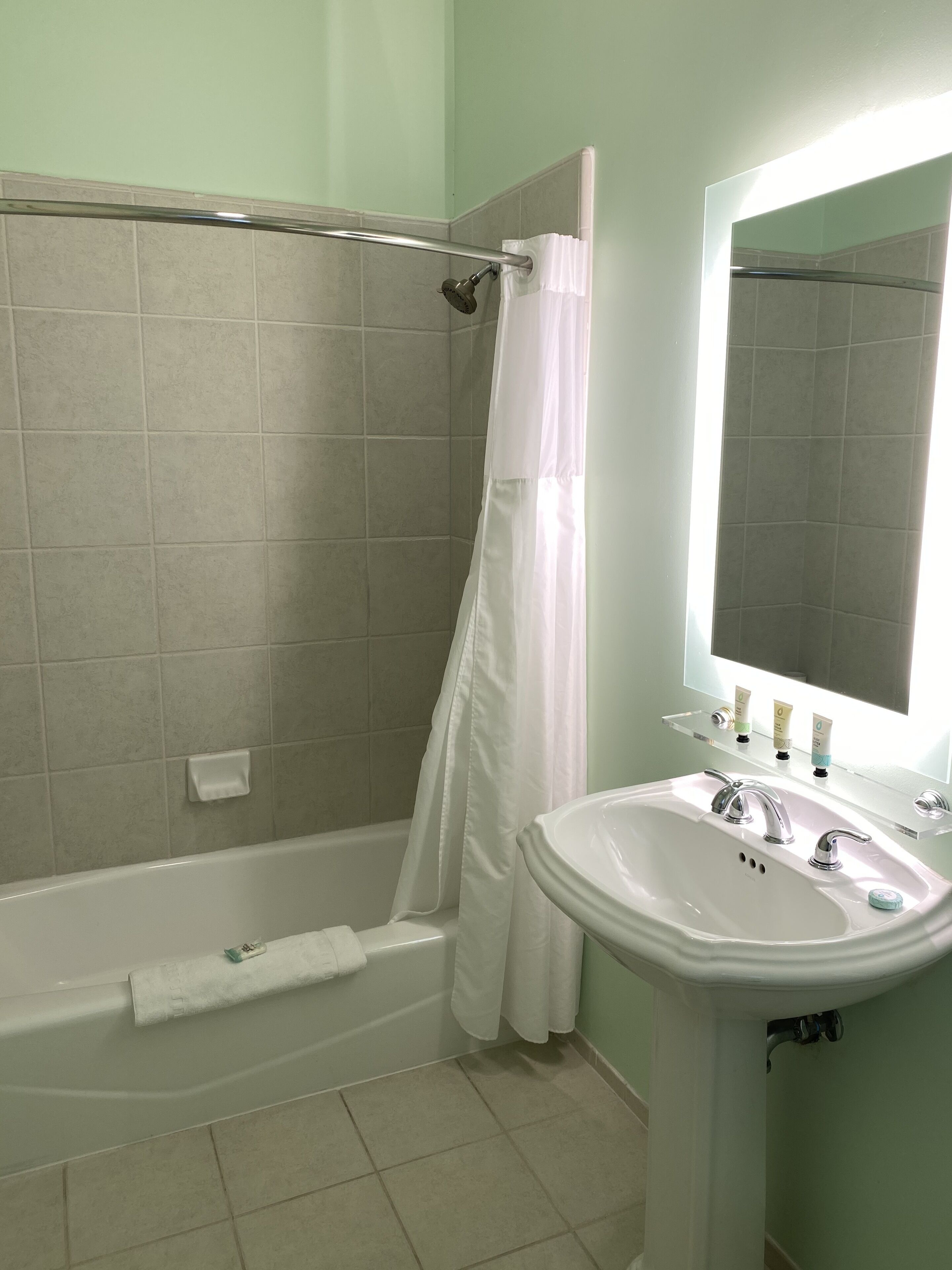 Un baño con bañera, cortina de ducha, lavamanos y espejo.