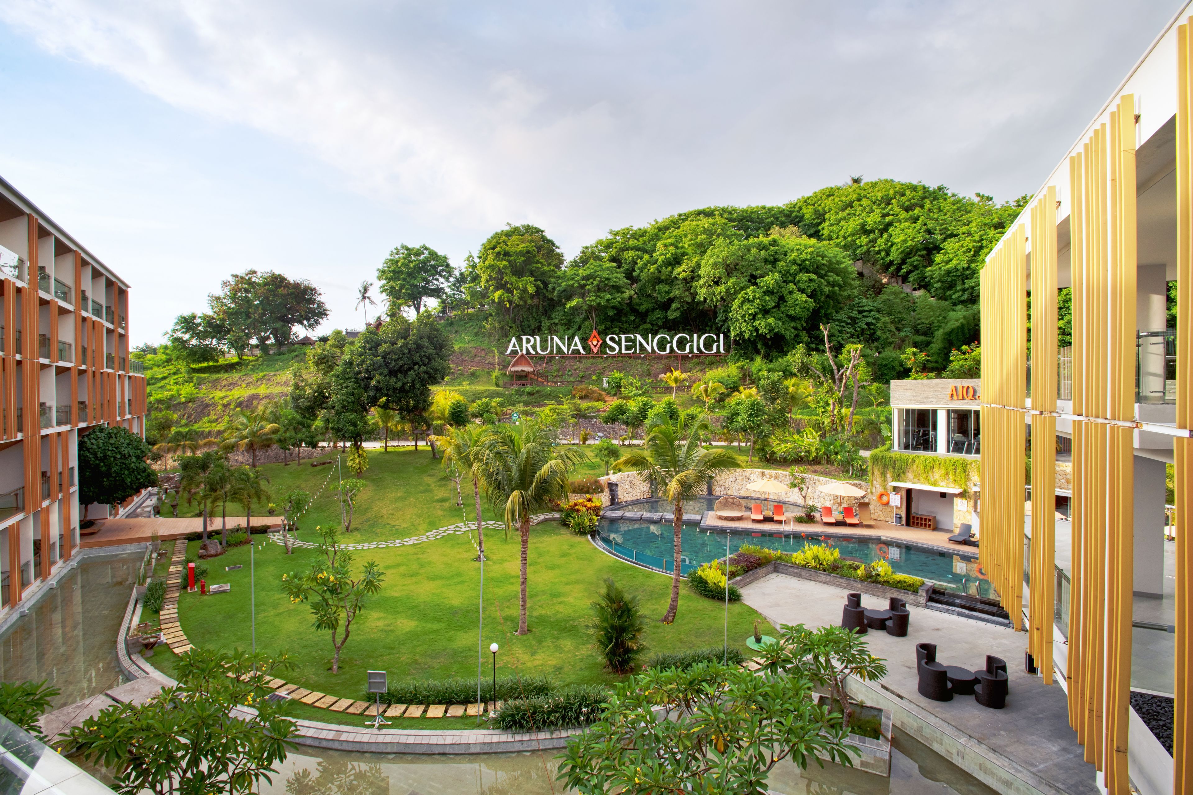 A modern hotel with a swimming pool, lush greenery, and a view of a hill.