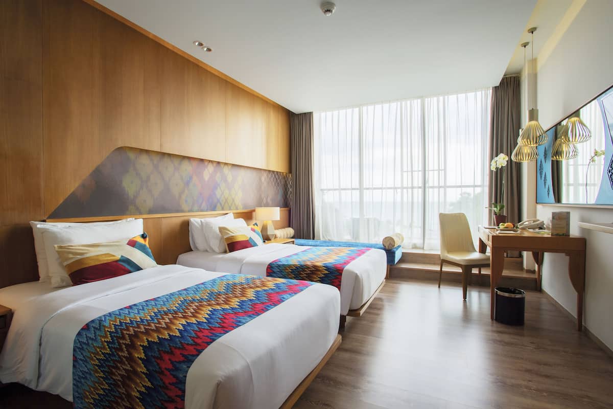 A hotel room with two beds, a desk, a chair, and a large window with curtains.