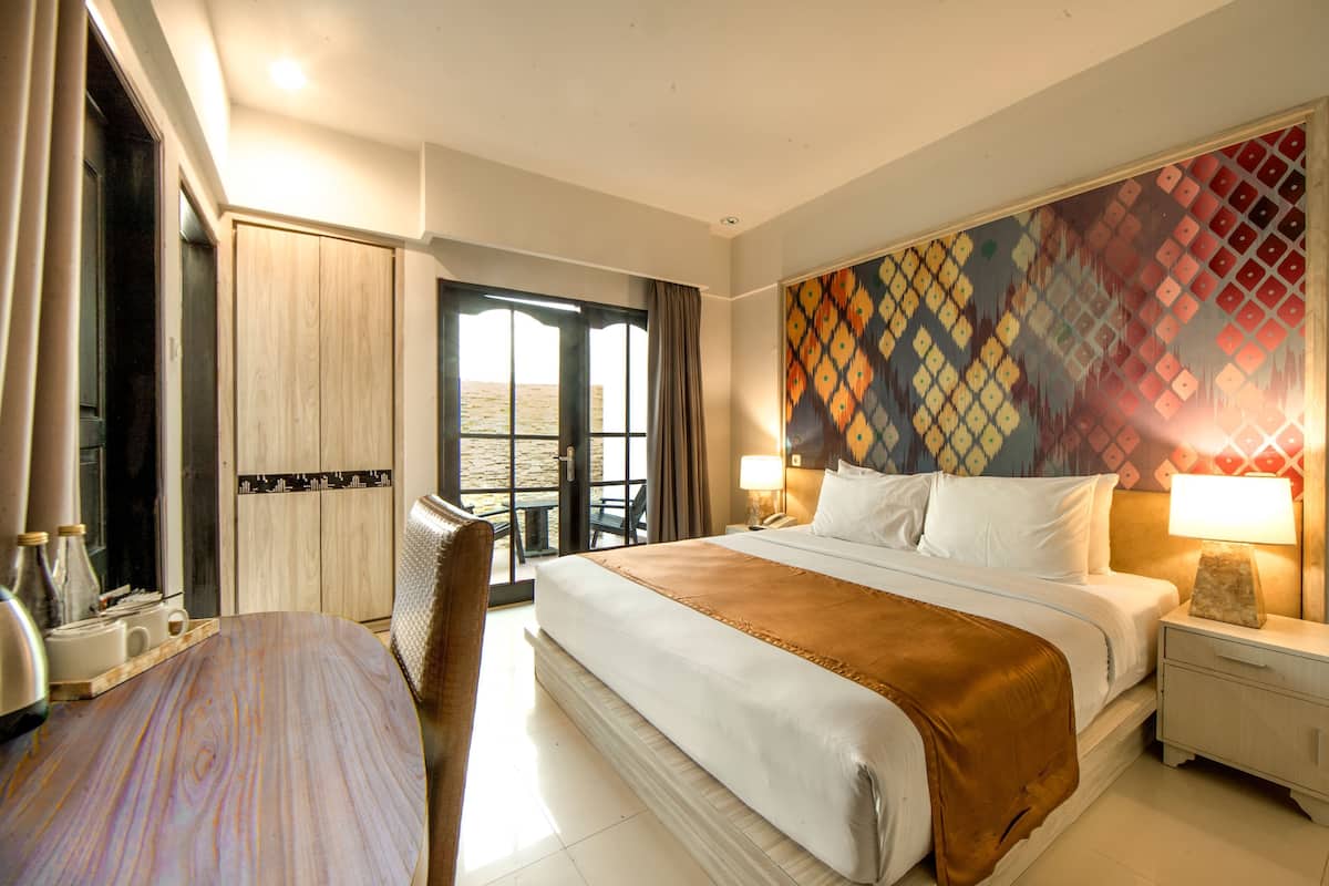 A hotel room with a large bed, a desk, a chair, and a view of the outdoors.