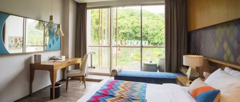Habitación de hotel con una cama grande, un escritorio, una silla, un ventanal con vistas a zonas verdes y un balcón.