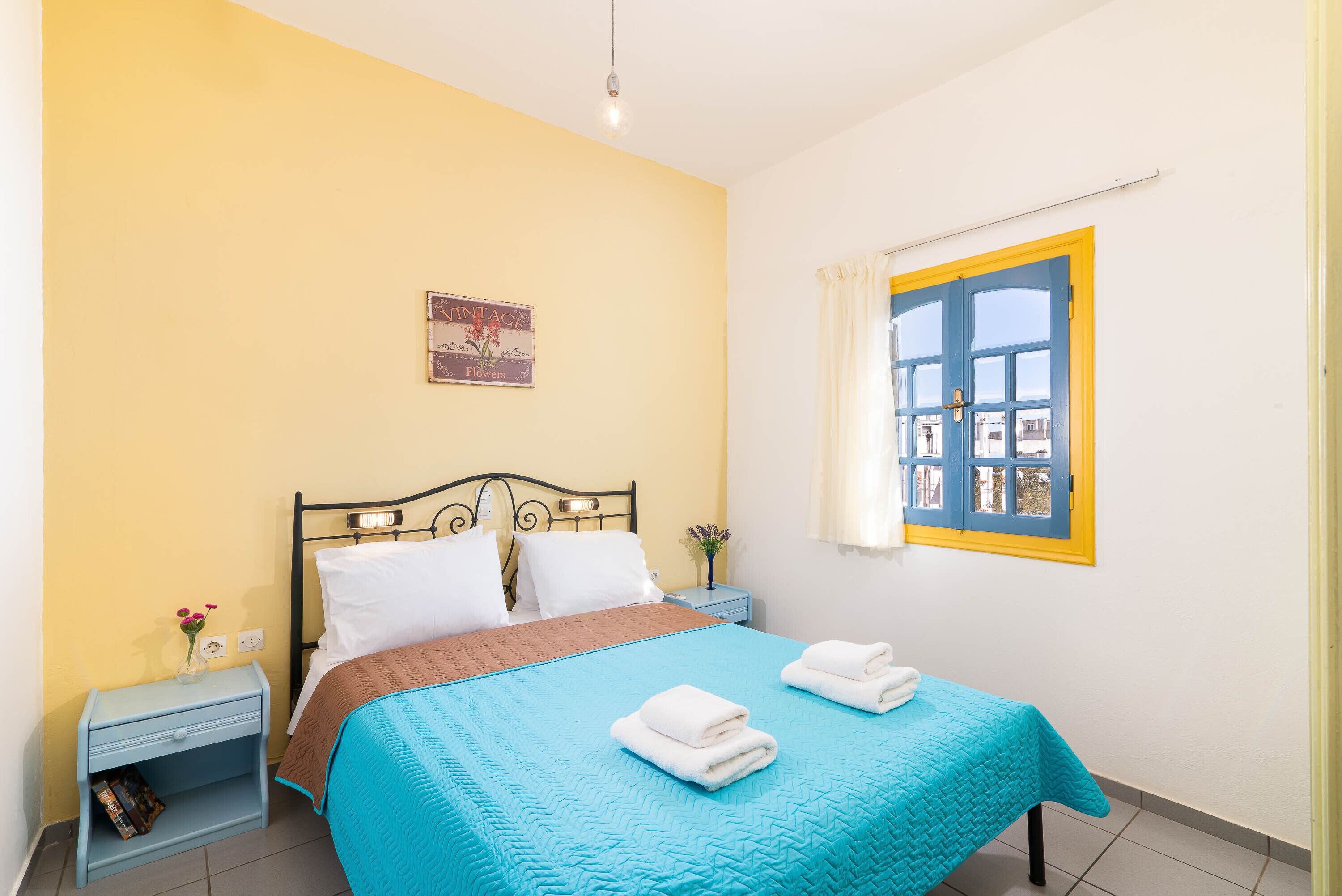 A bedroom with a bed, a nightstand, a window with curtains, and a wall-mounted picture.