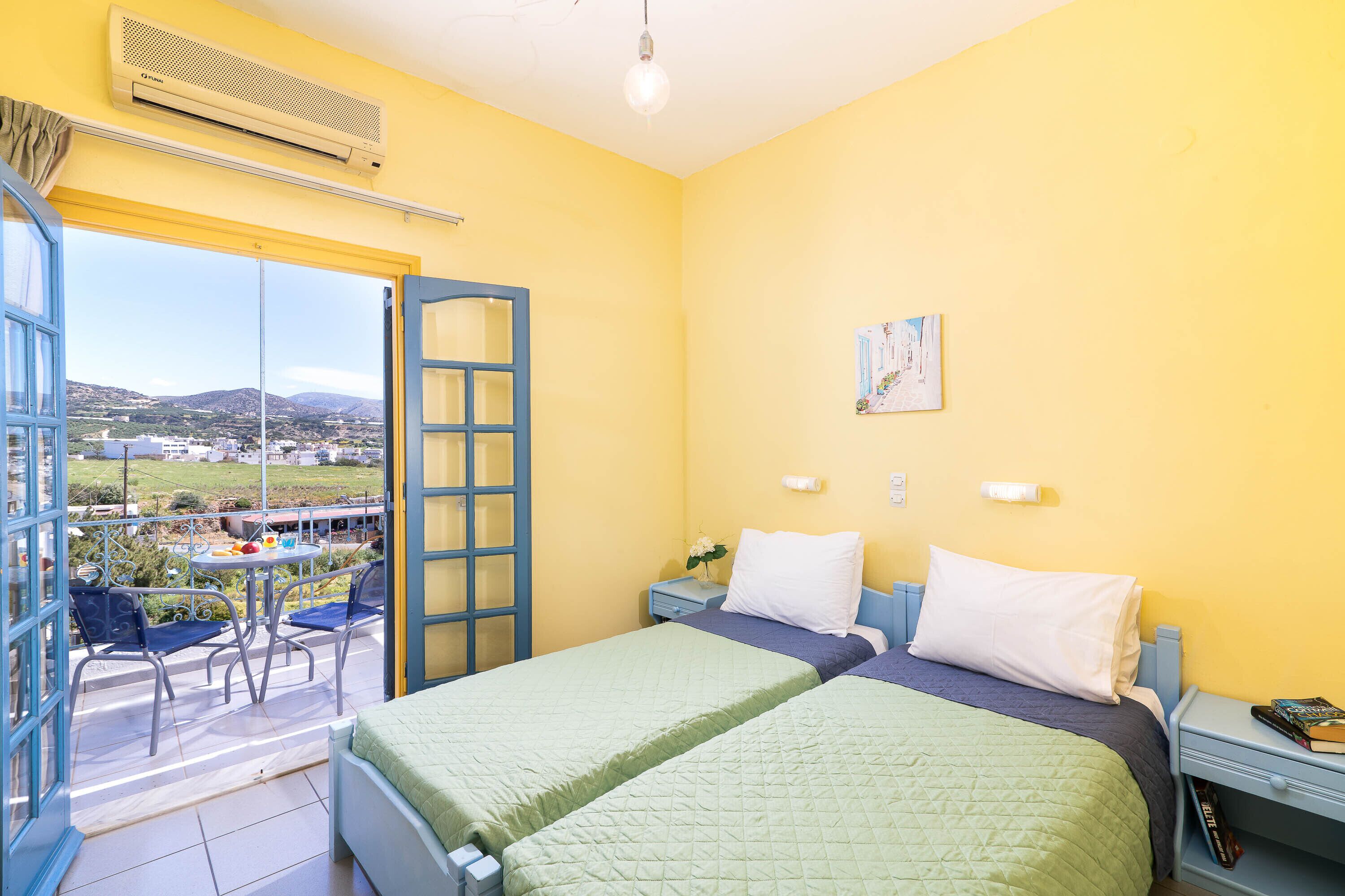 A room with two beds, a balcony with a table and chairs, and a view of the countryside.