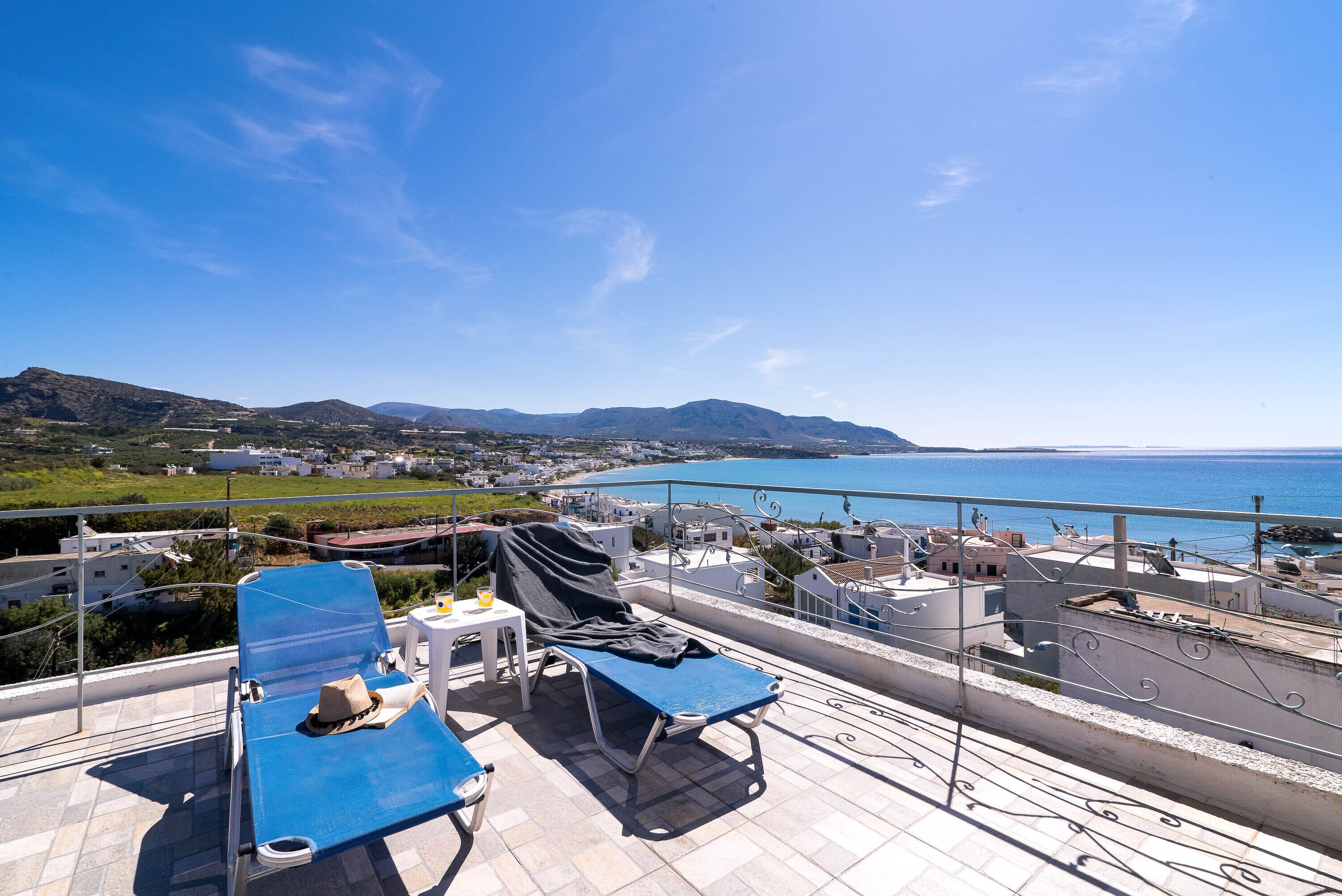 Un balcon équipé de deux chaises longues, d’une table et d’une chaise. La vue comprend une portion de côte et des bâtiments situés au loin.