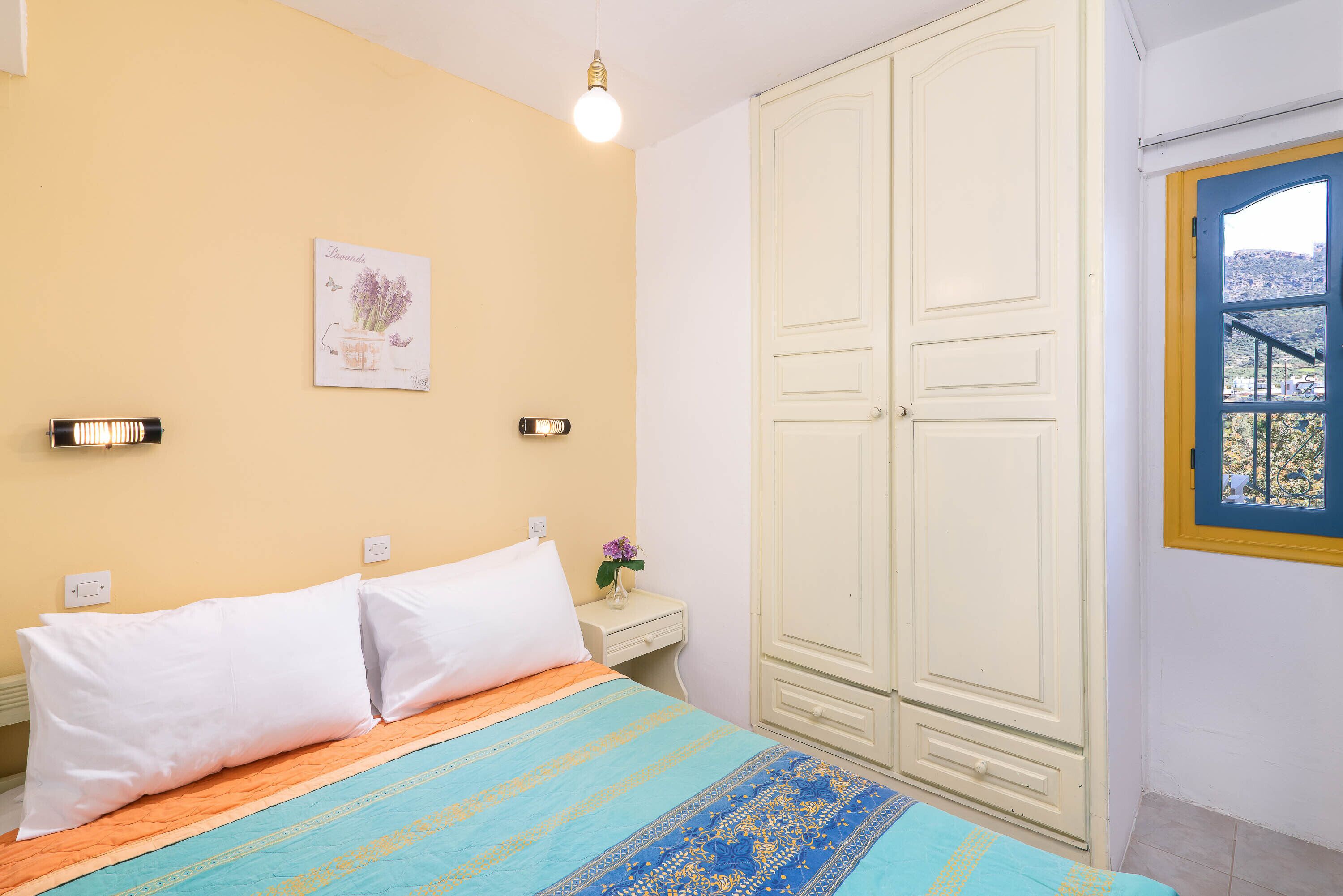 A bedroom with a bed, a nightstand, a wardrobe, and a window with a view.