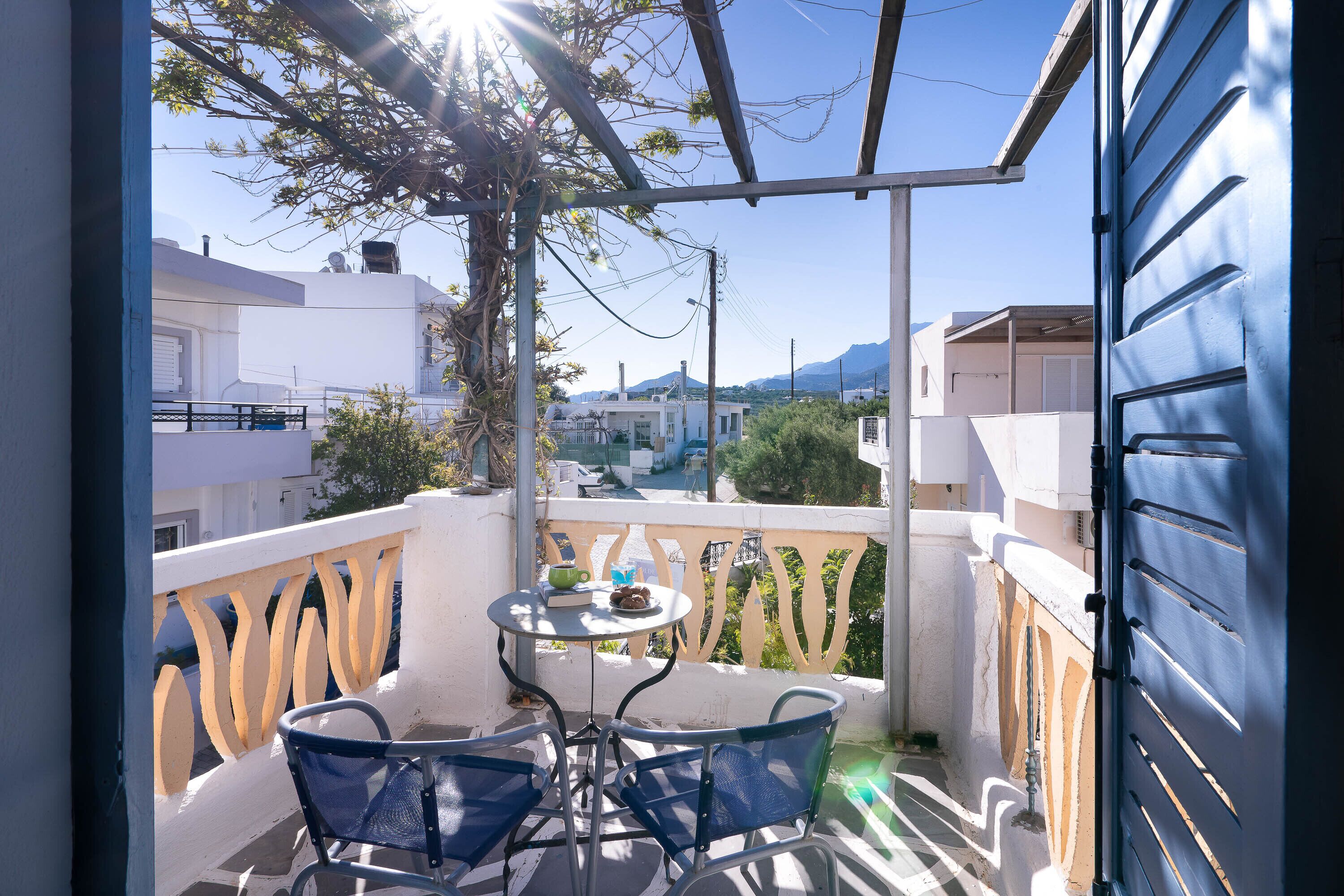 A balcony with a table and chairs, overlooking a residential area with white buildings and a clear sky.