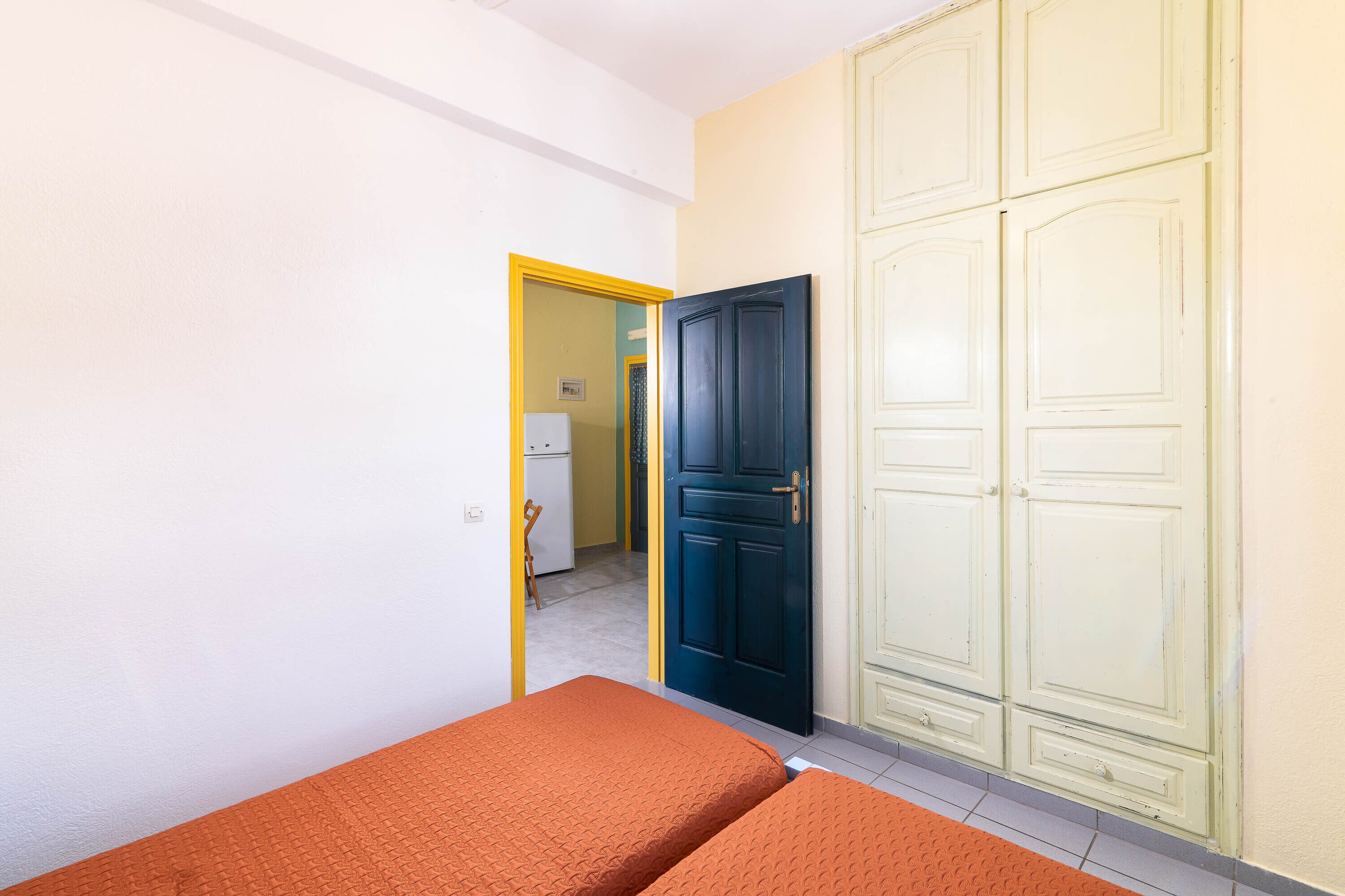 Ein Zimmer mit zwei Betten, einem Kleiderschrank und einer Tür zu einer Küche.