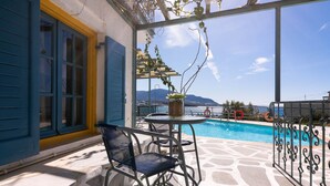 Terraço com piscina, persianas azuis e vista para as montanhas.