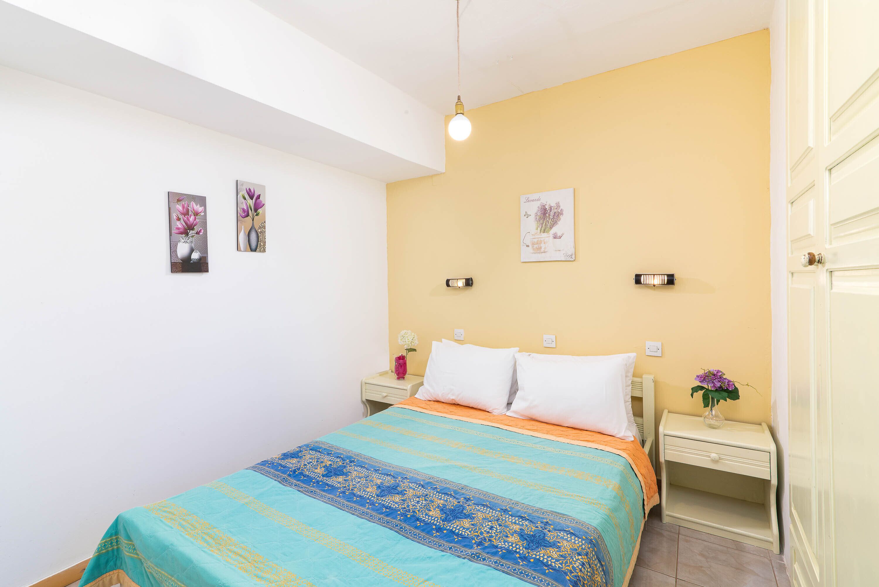 A bedroom with a bed, two bedside tables, a nightstand, and a wall-mounted light fixture.