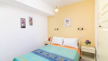A bedroom with a bed, two bedside tables, a nightstand, and a wall-mounted light fixture.