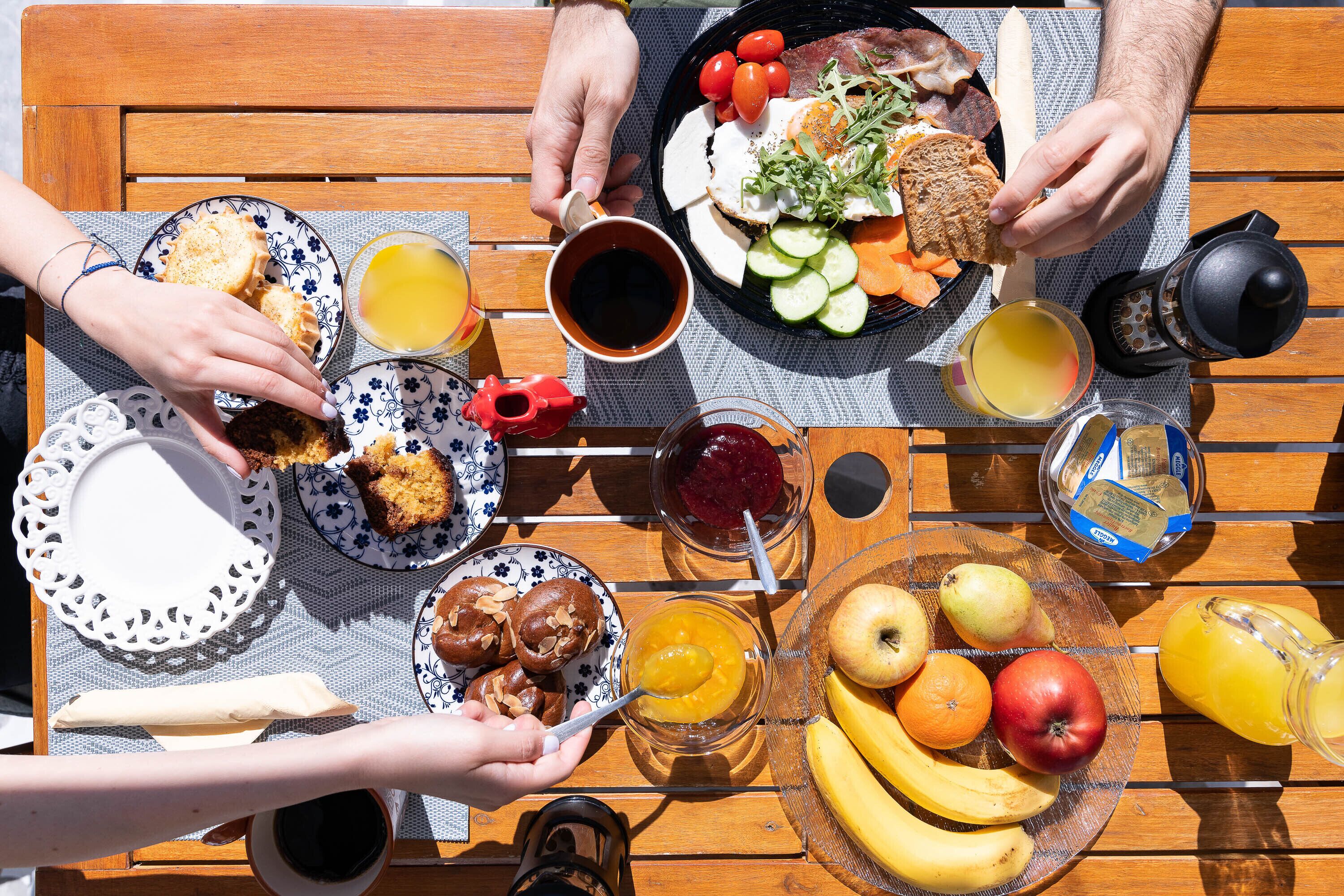 Una mesa de madera con diversos alimentos para el desayuno, como pan, fruta y bebidas.