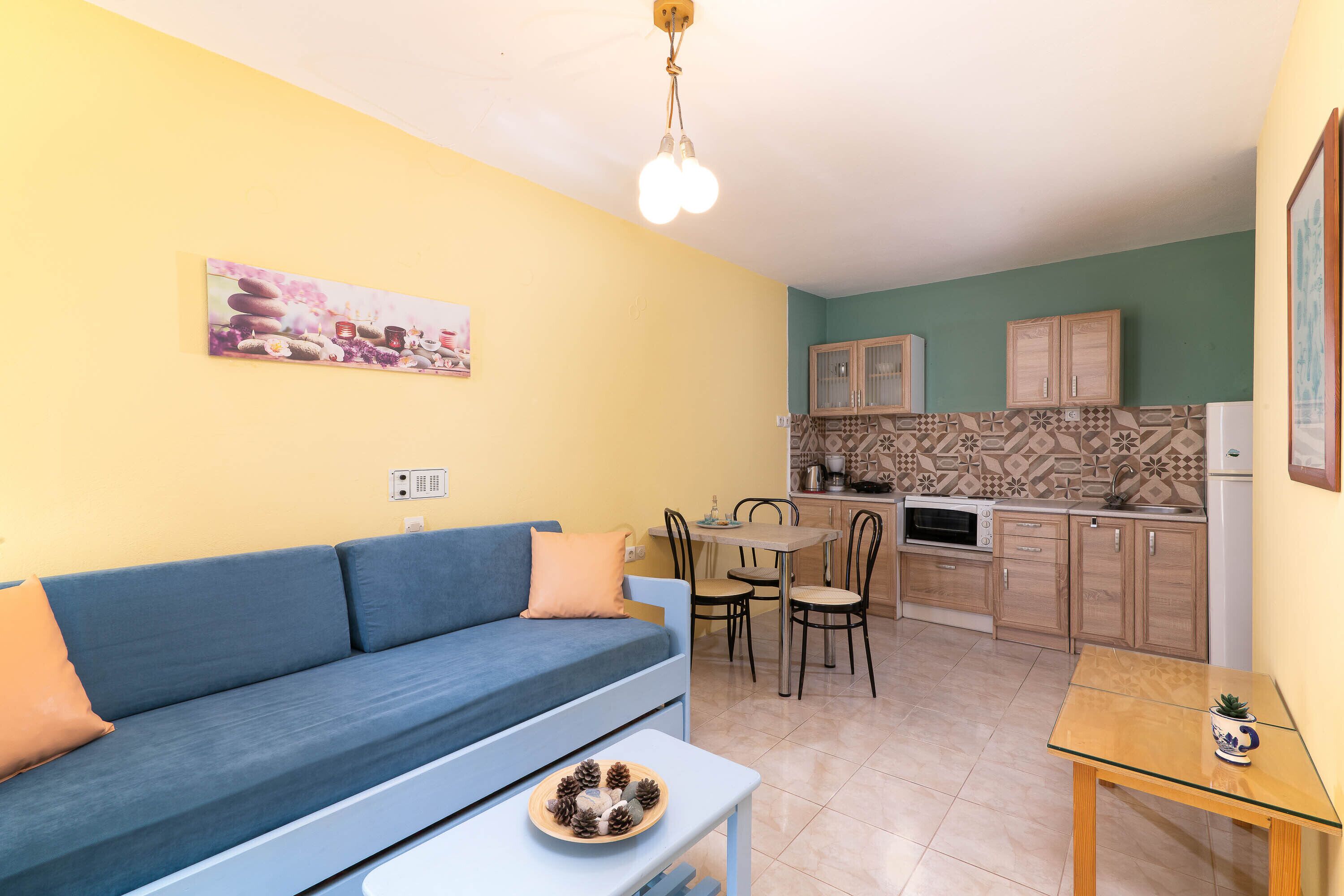 Un salon avec un canapé bleu, une petite table sur laquelle se trouve un bol rempli de pommes de pin, et un tableau accroché au mur.