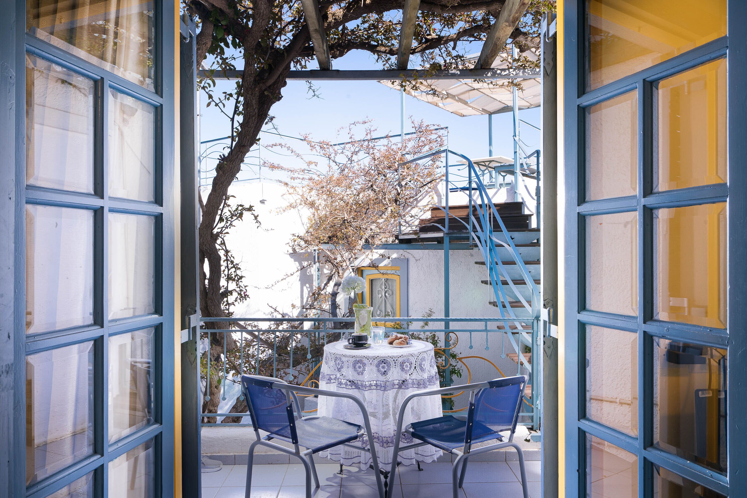 An outdoor balcony with a table and chairs, a tree, and a blue railing.