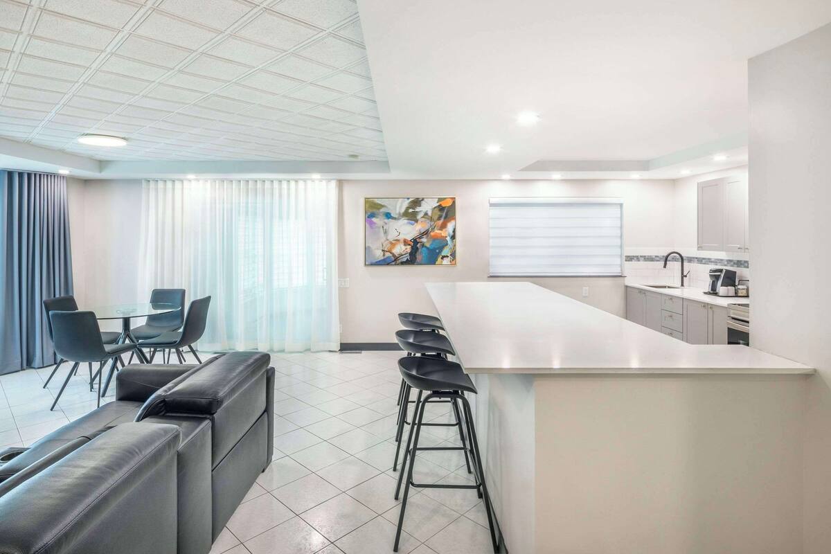 A modern kitchen with a central island, bar stools, and a dining area with a sofa and chairs.