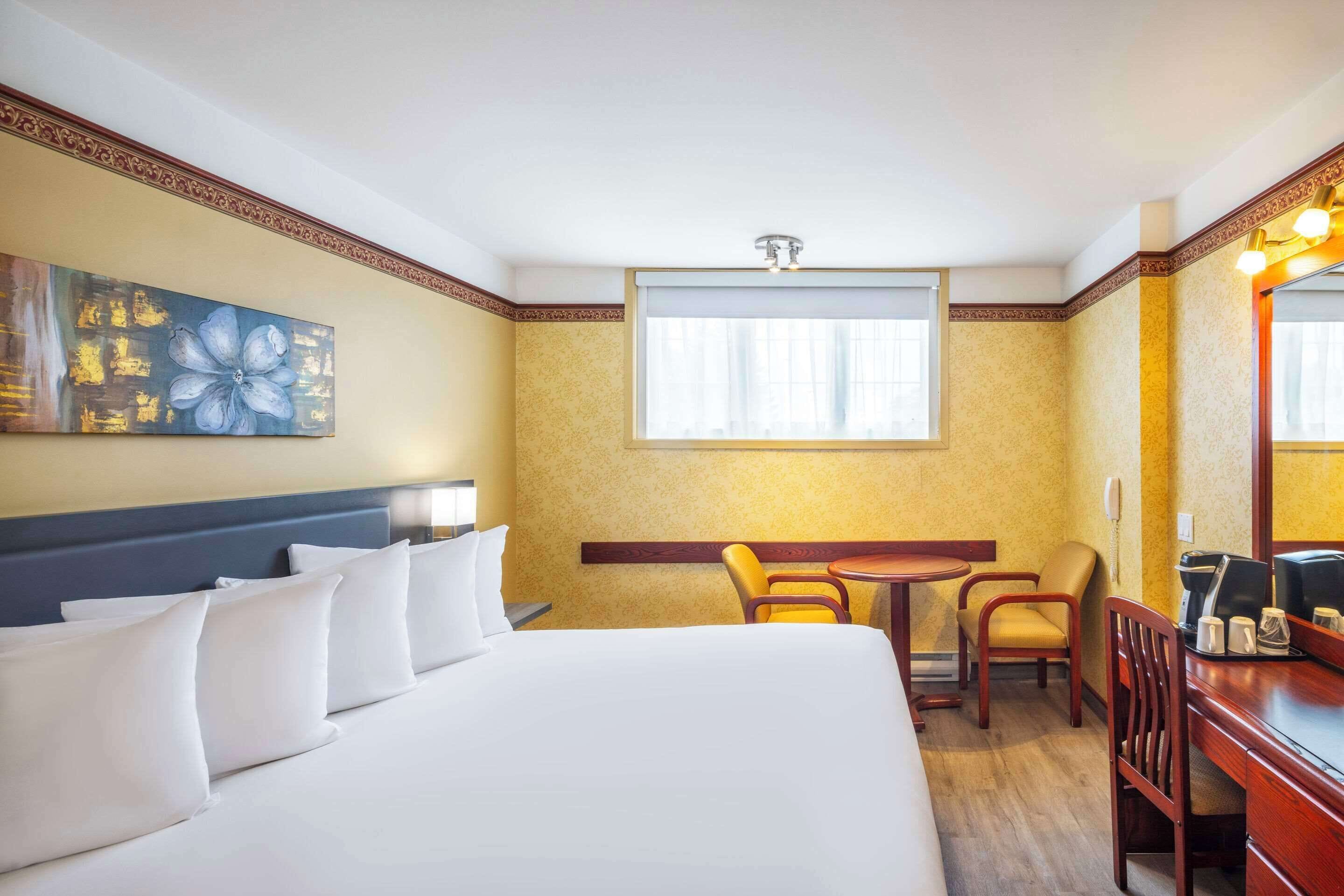 Habitación de hotel con una cama grande, un escritorio, dos sillas, una cafetera y un cuadro en la pared.